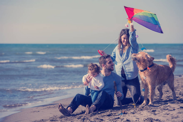 happy young family with kids having fun with a dog and  kite at beach during autumn day - Foto, imagen