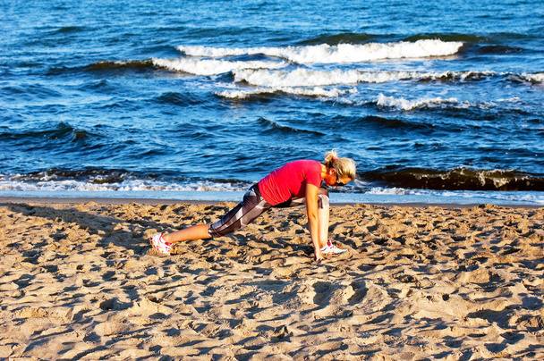 junge schöne Sportlerin macht Übungen am Strand - Foto, Bild
