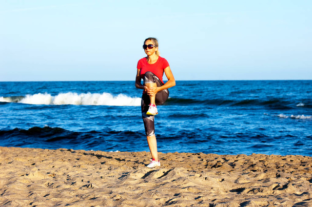 Young beautiful sportswoman doing exercises on beach - Photo, Image