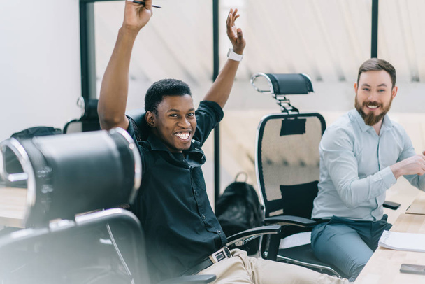 Portrait of happy african american student holding hands up and rejoicing completing task during private lesson with tutor.Two positive colleagues in formal wear celebrating victory of common project - Fotoğraf, Görsel