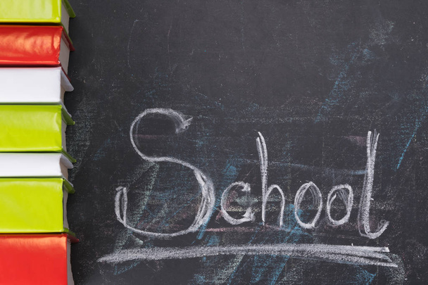 on the chalkboard written the word school and on the left vertically lie in a row of books - 写真・画像