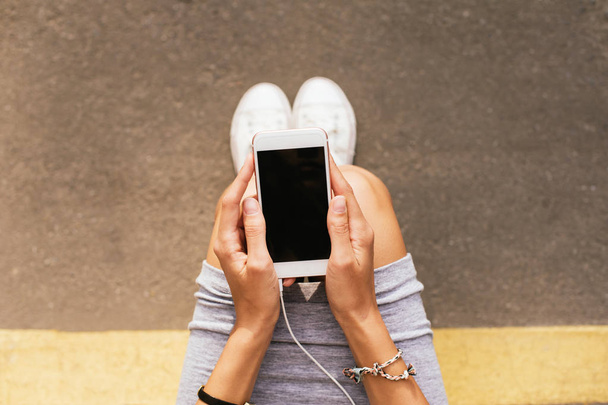Girl in sneakers sitting on the floor with smart phone in her hands. - Foto, imagen