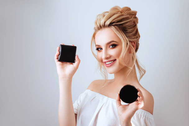 Fashion glamour portrait of happy smiling blonde woman long wavy hair style holding cosmetics over light studio background. Beautiful face Make up product cosmetics. - Foto, Imagen