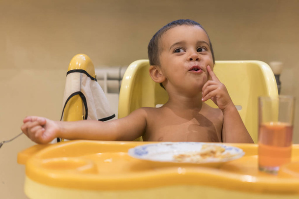 食べる 2 歳の少年。子供用テーブル。子どもの自立の概念。スプーンでかわいい幼児少年はヨーグルトです。子供の笑顔。ベビーシートで面白い子供 - 写真・画像