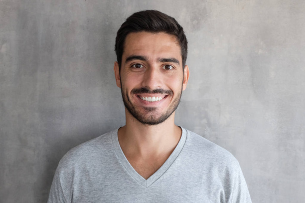 Close up shot of young smiling man standing against gray textured wall - Φωτογραφία, εικόνα