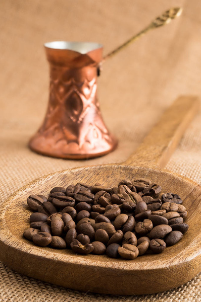 Grãos de café torrados em concha de madeira e panela de café de bronze tradicional em pano de saco
 - Foto, Imagem