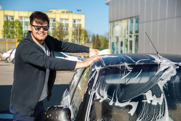 young man in sunglasses washing car at self service carwash - Foto, Bild