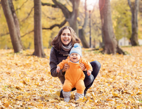 Mother playing in park with her toddler baby. Mom and son over seasonal autumn background. Love and family concept. - Фото, зображення