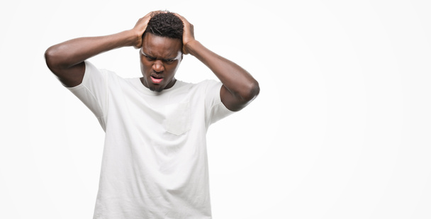Młody człowiek african american noszenia biały t-shirt cierpiących ból głowy, zdesperowany i zestresowani, bo bóle i migreny. Ręce na głowę. - Zdjęcie, obraz