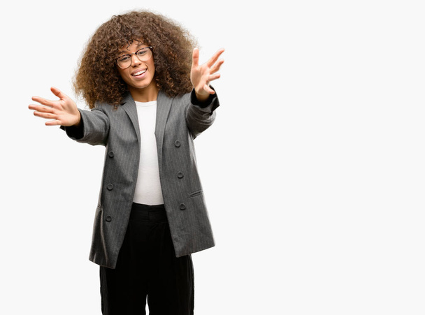 Mulher de negócios afro-americana usando óculos olhando para a câmera sorrindo de braços abertos para abraço. Expressão alegre abraçando a felicidade
. - Foto, Imagem