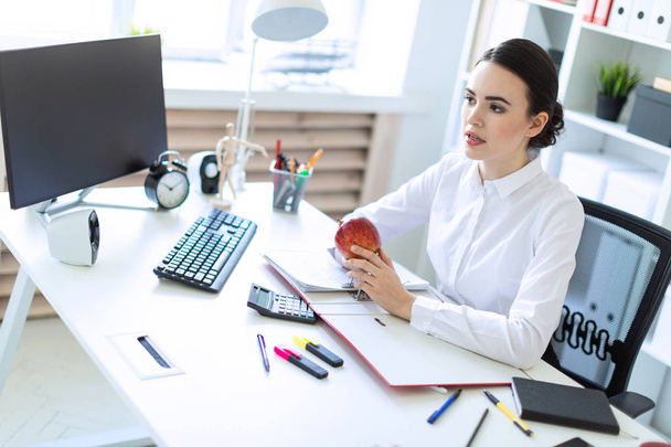 Young girl in the office working with documents and holding an apple. - Фото, зображення