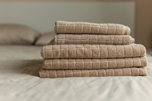 Stack of beige hotel towel on bed in bedroom interior. Soft focus. - Photo, image