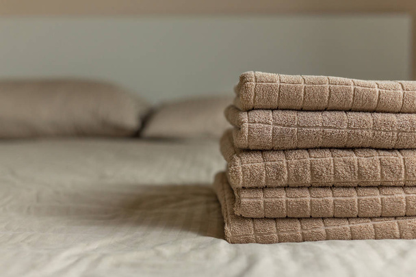 Stack of beige hotel towel on bed in bedroom interior. Soft focus. - Fotó, kép