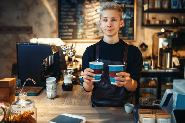 Male barista holds in hands two cups of fresh hot coffee, cafe counter on background. Professional espresso preparation by barman in cafeteria, bartender occupation - Фото, зображення