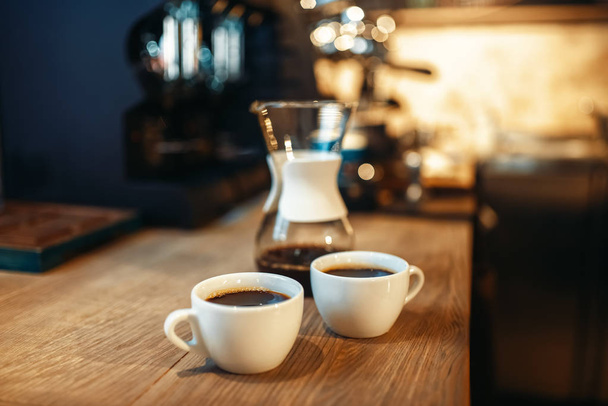 Две чашки свежего черного кофе стоят на деревянном столике в кафе эспрессо, интерьер кафетерия на заднем плане, никто
 - Фото, изображение