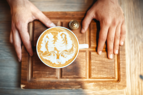 Erkek barista kahve köpüğü çizim, üstten görünüm, ahşap kafe tezgahın üzerine arka plan ile tutar. Barmen barmen sanat işgal kafeteryasında tarafından profesyonel kapuçino hazırlık - Fotoğraf, Görsel