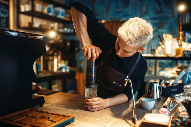 Jovem barista masculino faz café expresso fresco, preparação de café preto no balcão do café. Barman trabalha em cafetaria, profissão de barman
 - Foto, Imagem