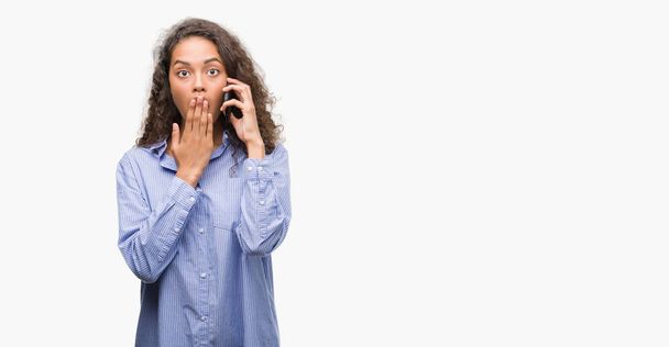 Young hispanic woman using smartphone cover mouth with hand shocked with shame for mistake, expression of fear, scared in silence, secret concept - Fotoğraf, Görsel