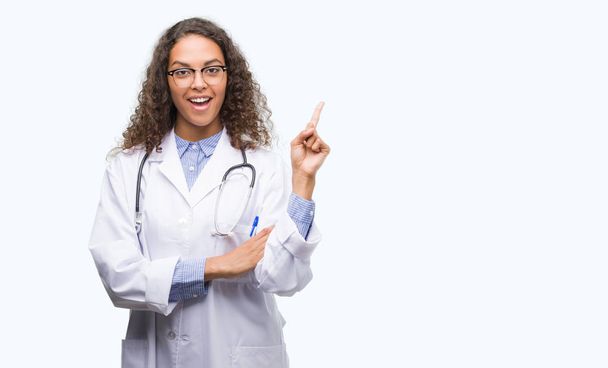 Młody lekarz hiszpanin kobieta bardzo szczęśliwy, wskazując z dłoni i palców z boku - Zdjęcie, obraz