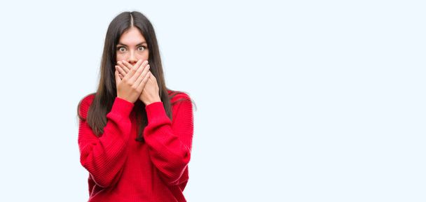 junge schöne hispanische tragen roten Pullover schockiert bedeckt Mund mit den Händen für Fehler. Geheimes Konzept. - Foto, Bild