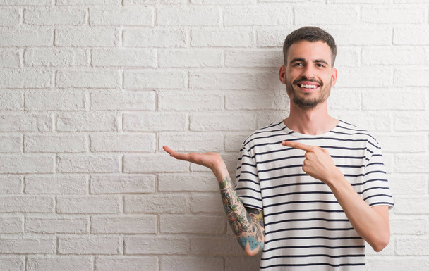 Giovane uomo adulto in piedi sopra muro di mattoni bianchi molto felice puntando con mano e dito
 - Foto, immagini