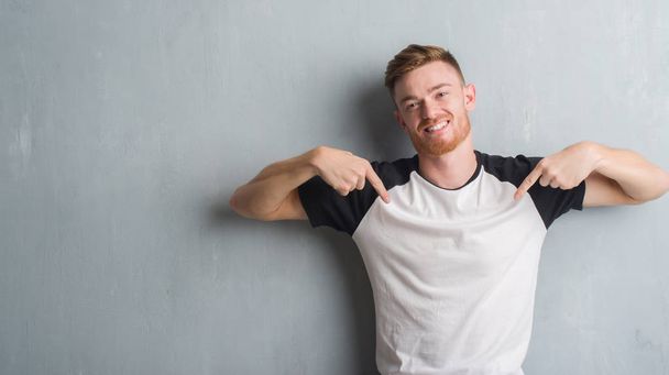 Young redhead man over grey grunge wall looking confident with smile on face, pointing oneself with fingers proud and happy. - Photo, Image