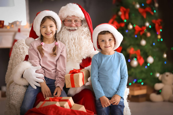 Little children receiving gifts from authentic Santa Claus indoors - Foto, Imagen