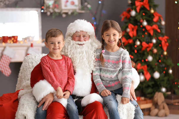 Little children sitting on authentic Santa Claus' knees indoors - Foto, afbeelding