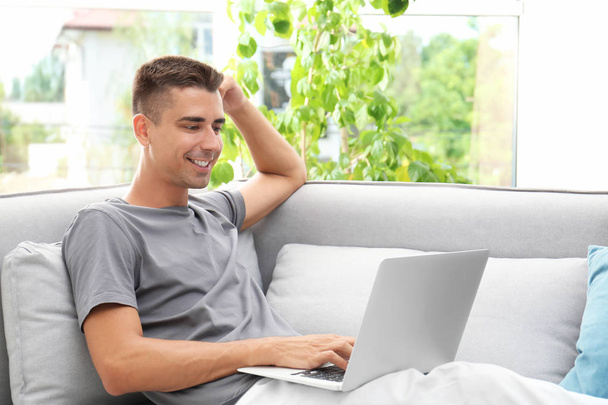 Man in casual clothes using laptop on sofa at home - Foto, Imagen