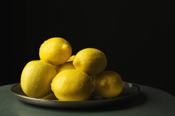 Plate with whole lemons on small table against dark background - Φωτογραφία, εικόνα