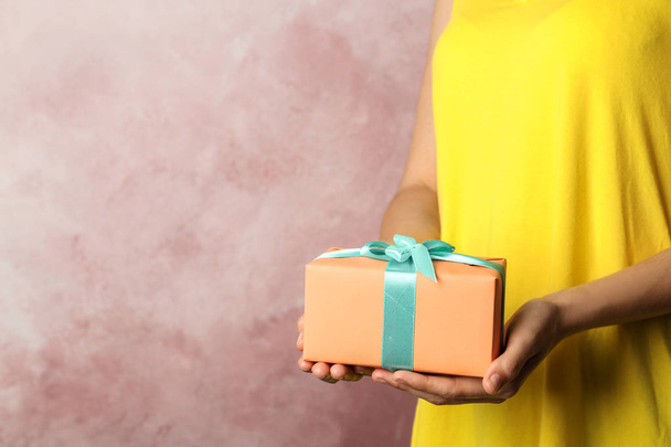 Woman holding beautifully wrapped gift box on color background - Photo, image