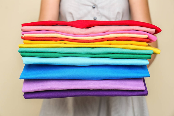Woman holding stack of colorful t-shirts on light background - Zdjęcie, obraz