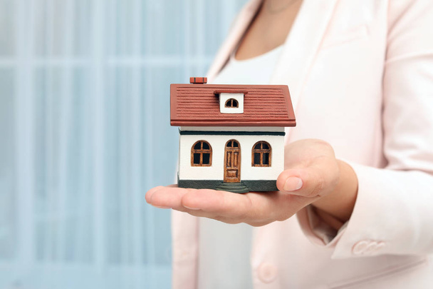Real estate agent holding house model on blurred background - Foto, Imagen