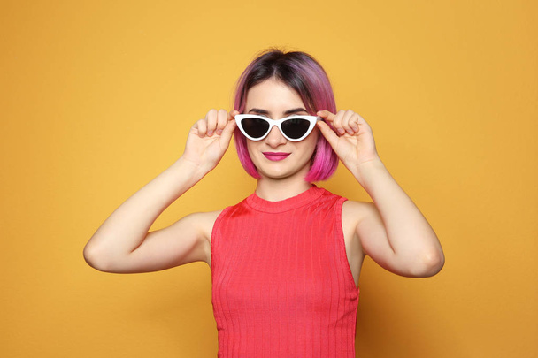 Young woman with trendy hairstyle wearing sunglasses against color background - Photo, image