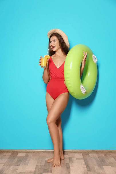 Beautiful young woman with inflatable ring and glass of cocktail near color wall - 写真・画像