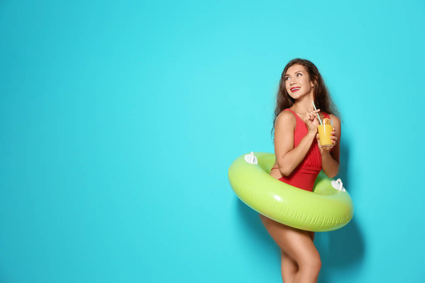 Beautiful young woman with inflatable ring and glass of cocktail on color background - Фото, изображение