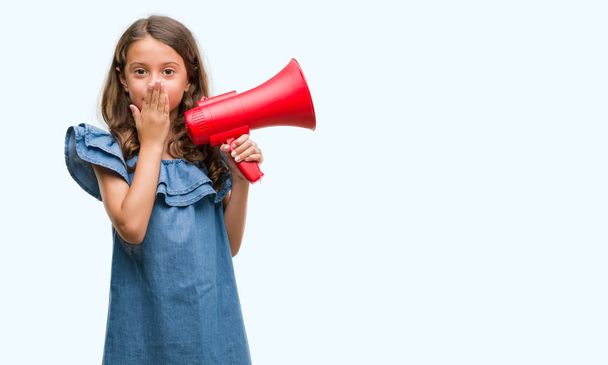 Brunette hispanic girl holding red megaphone cover mouth with hand shocked with shame for mistake, expression of fear, scared in silence, secret concept - Foto, Imagem