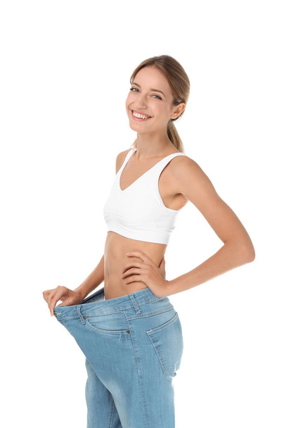 Young slim woman in old big jeans showing her diet results on white background - Zdjęcie, obraz