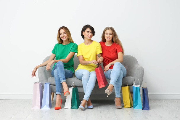 Group of young women with shopping bags sitting on sofa near light wall - Fotografie, Obrázek