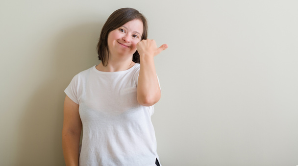 Frau mit Down-Syndrom, die über der Wand steht, mit glücklichem Gesicht lächelt und mit erhobenem Daumen zur Seite zeigt. - Foto, Bild
