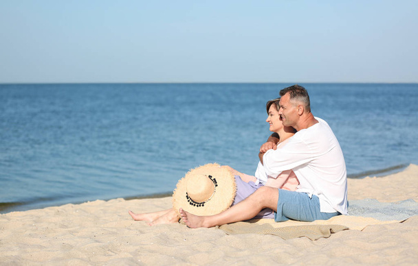 Happy mature couple sitting together at beach on sunny day - Foto, Imagem