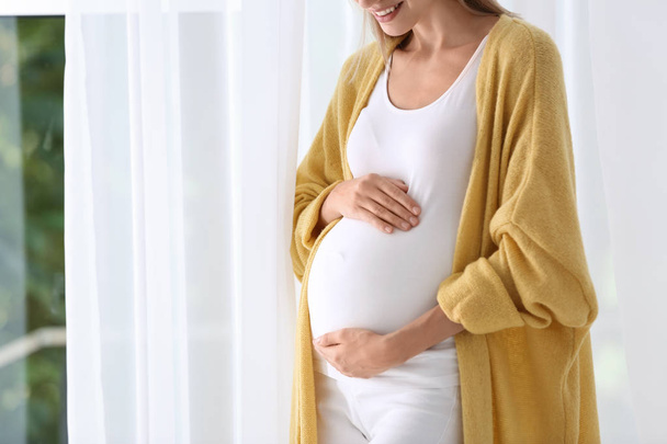 Pregnant woman standing near window at home, closeup - Фото, зображення