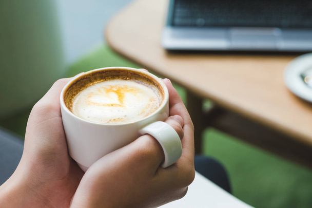 Close-up van de hand met hete koffie cappuccino-kop met hart latte art in café winkel, vrijetijdsbesteding - Foto, afbeelding