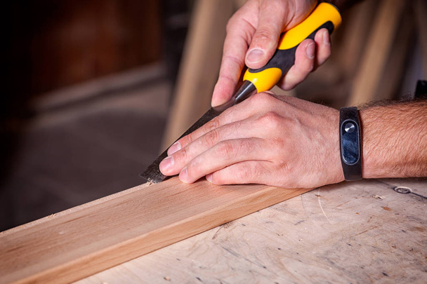 Крупным планом молодой человек-строитель обрабатывает деревянный продукт зубилом в мастерской
 - Фото, изображение