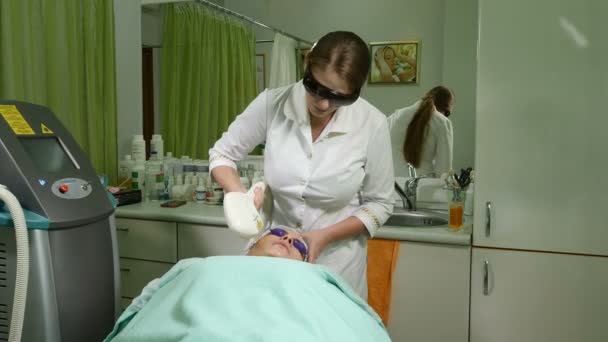 Hautpflege. Frau mit Brille auf Augen bekommt Foto-Verjüngungskur in einem Schönheitssalon. Kosmetikerin, die Gesichtsbehandlung durchführt. Schuss in 4k - Filmmaterial, Video