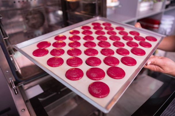 Professional baker putting baking pan with pink macaroons - Foto, imagen