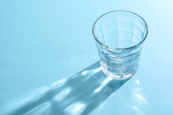 Transparent glass Cup on blue background and long shadow from it with different pictures - Fotoğraf, Görsel