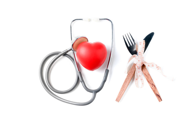 Красное сердце и стетоскоп с измерительной лентой вокруг вилки и ножа изолированы на белом фоне, здравоохранение и диета концепции
 - Фото, изображение