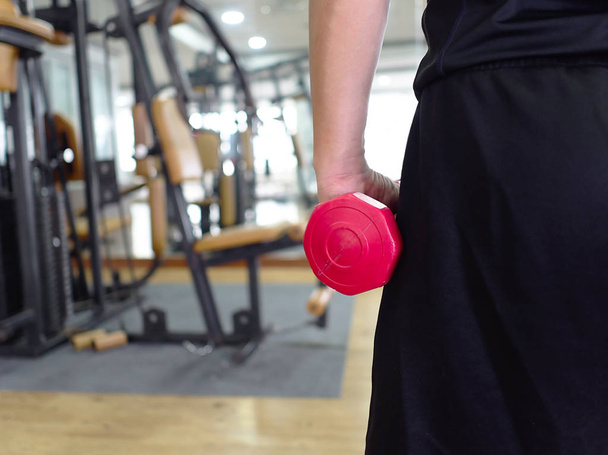 Back view of healthy young man holding dumbbell at sport gym. Fitness and workout concept - Zdjęcie, obraz