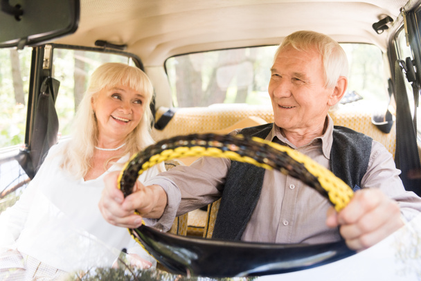 Schönes Seniorenpaar lächelt und fährt beiges Auto - Foto, Bild